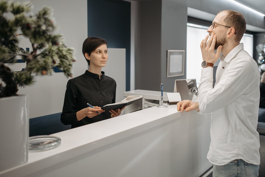 A receptionist assists a patient with a toothache at a dental clinic's front desk.